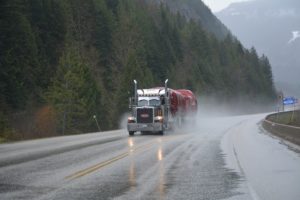 Large semi truck on wooded highway.